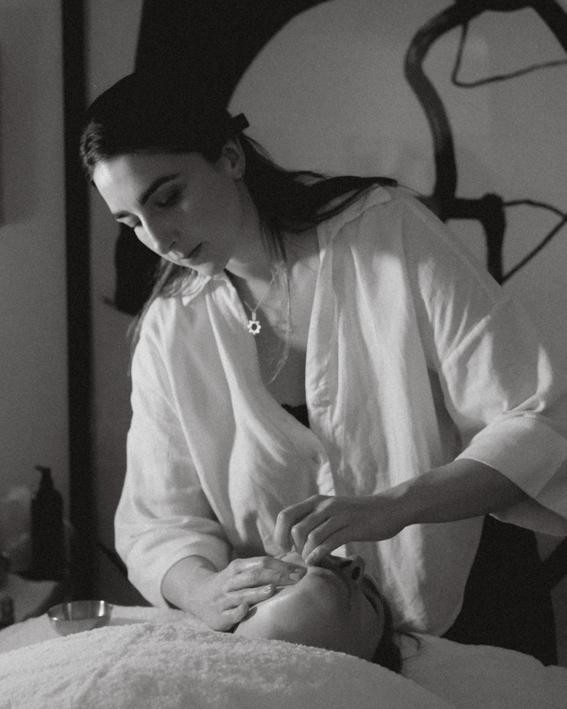 Facialist Katie England performing a facial massage on a client during a skincare treatment, black and white photography