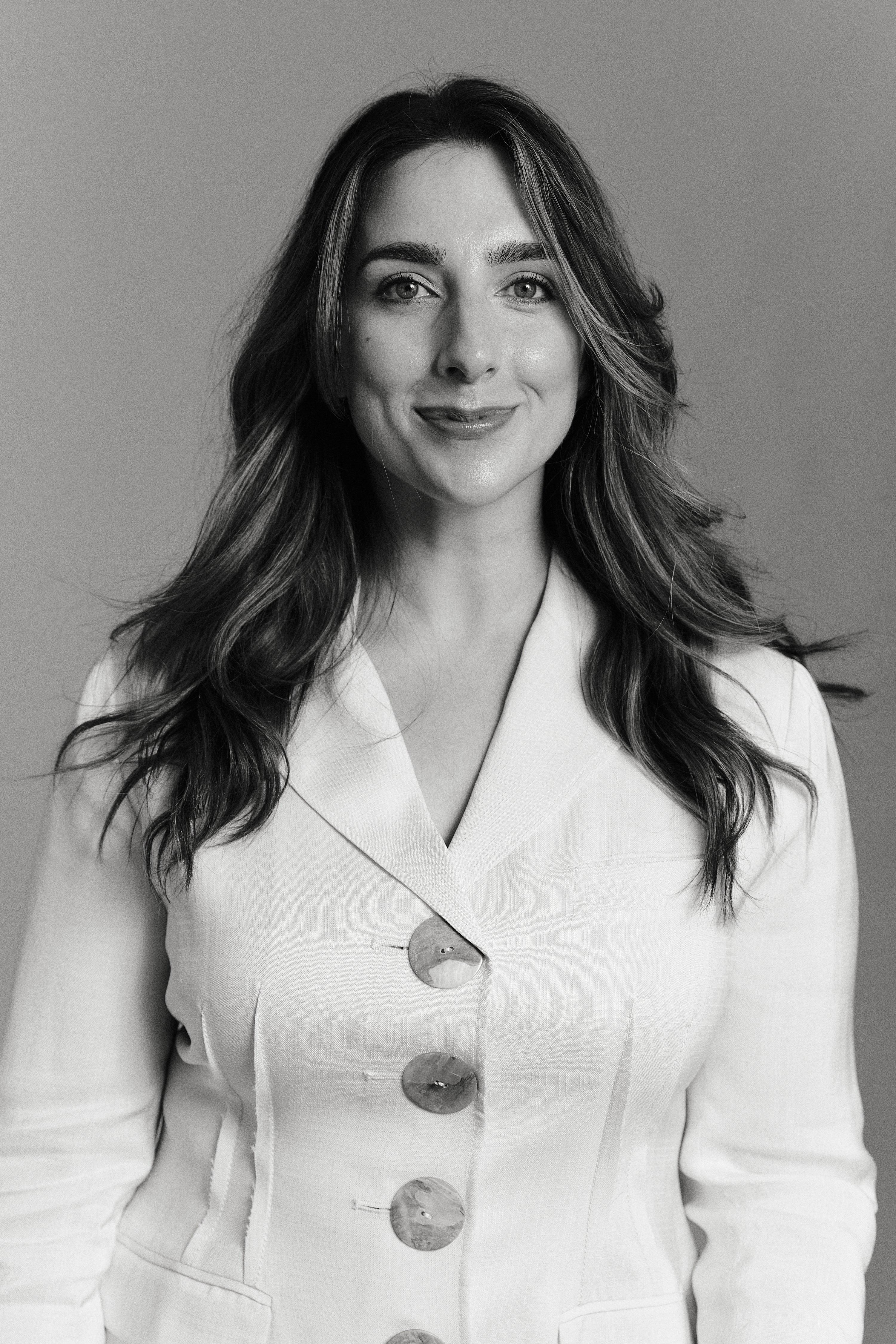 Facialist Katie England smiling in a white blazer, black and white headshot portrait