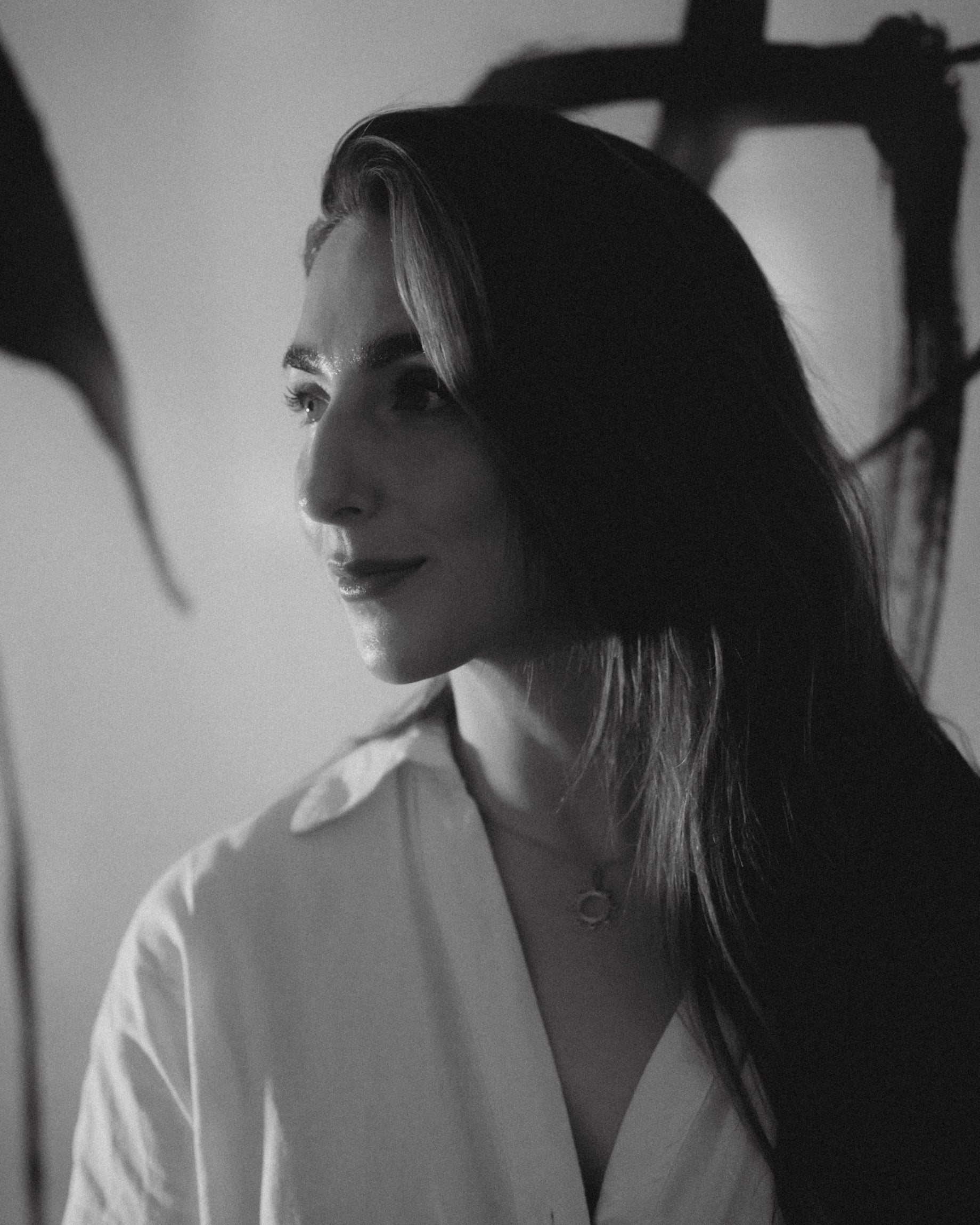 Soft profile portrait of facialist Katie England in a white linen shirt with abstract artwork in the background, black and white photography