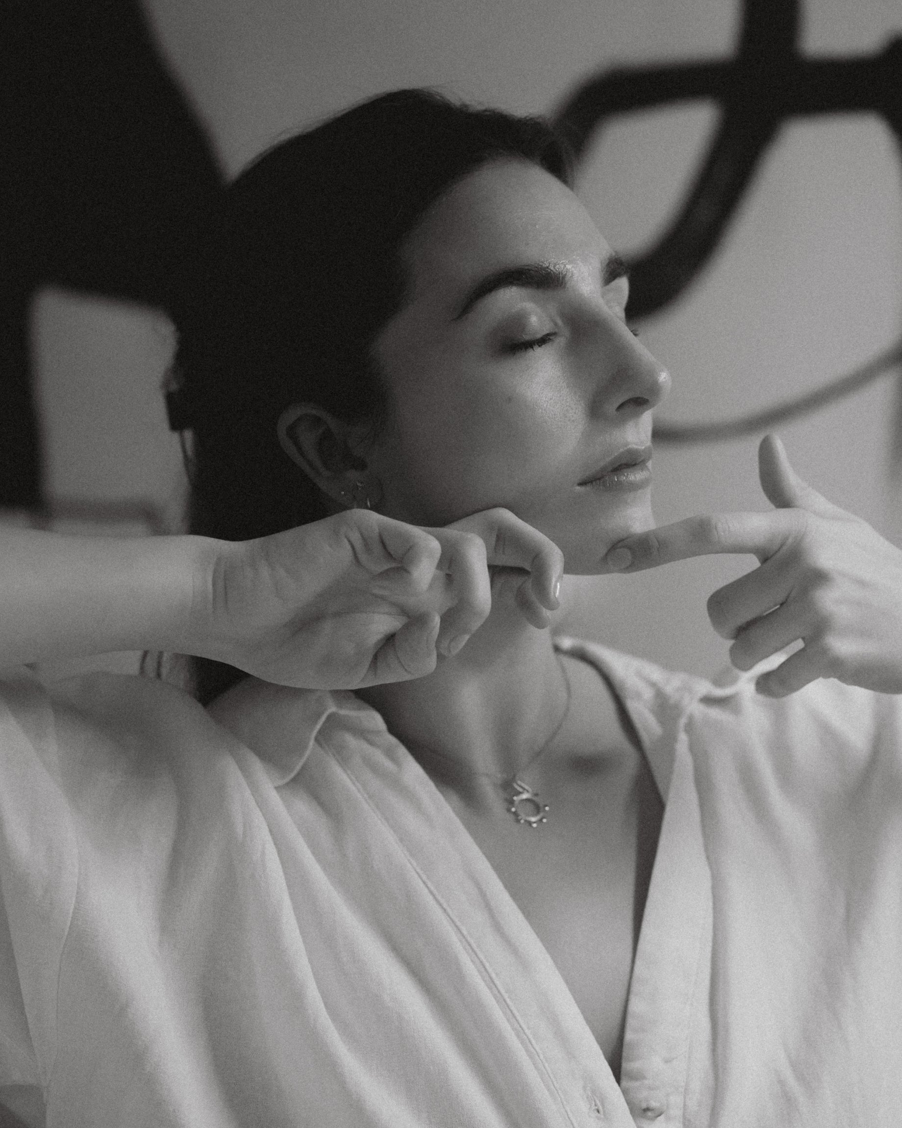 Katie England demonstrating a jawline sculpting technique with eyes closed, black and white portrait