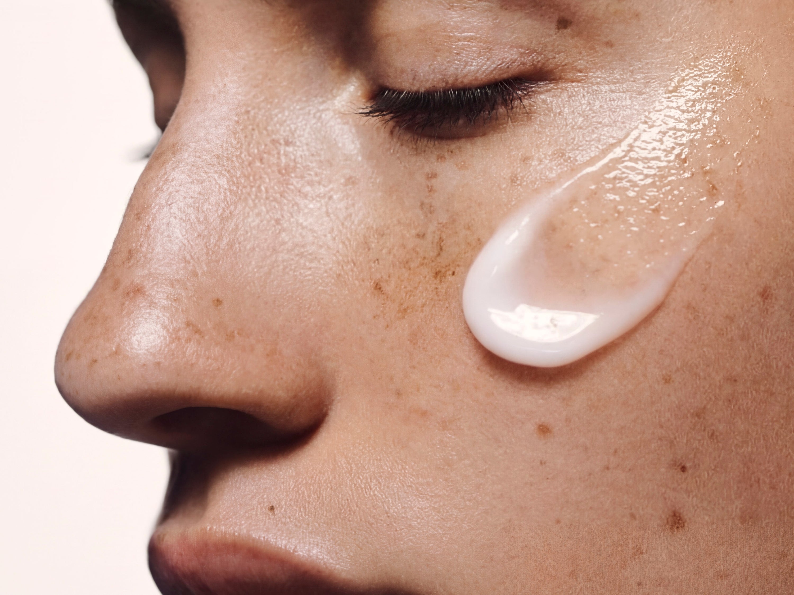 Close-up of a white moisturiser swatch on a freckled cheek, showing rich cream texture